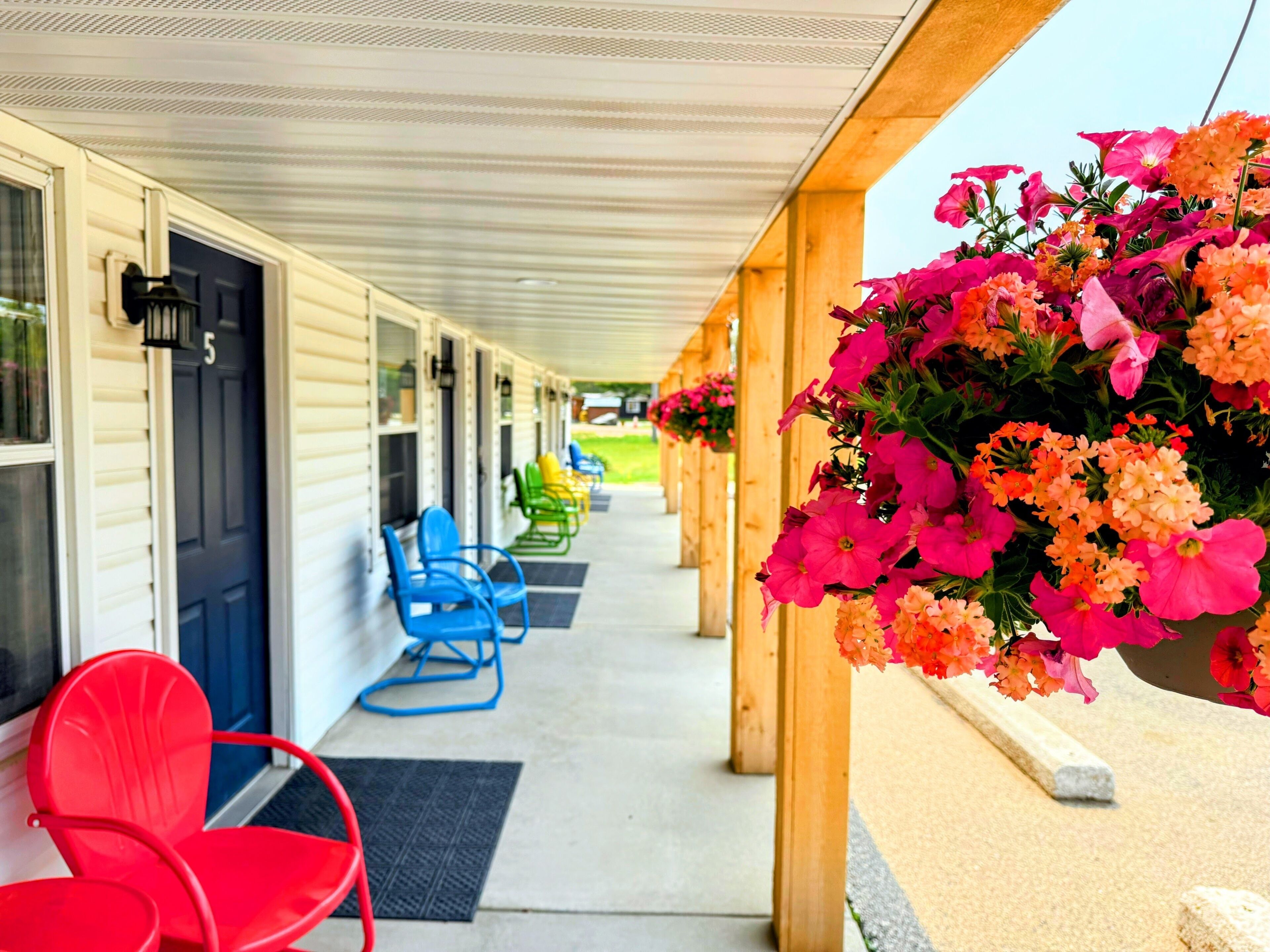 Ein Motel mit überdachter Veranda, Sitzgelegenheiten im Freien und hängenden Blumenkörben.