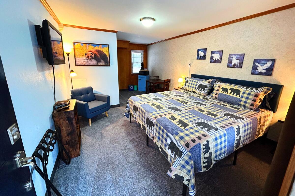 Un dormitorio con una cama grande, una silla, un escritorio y un televisor montado en la pared.