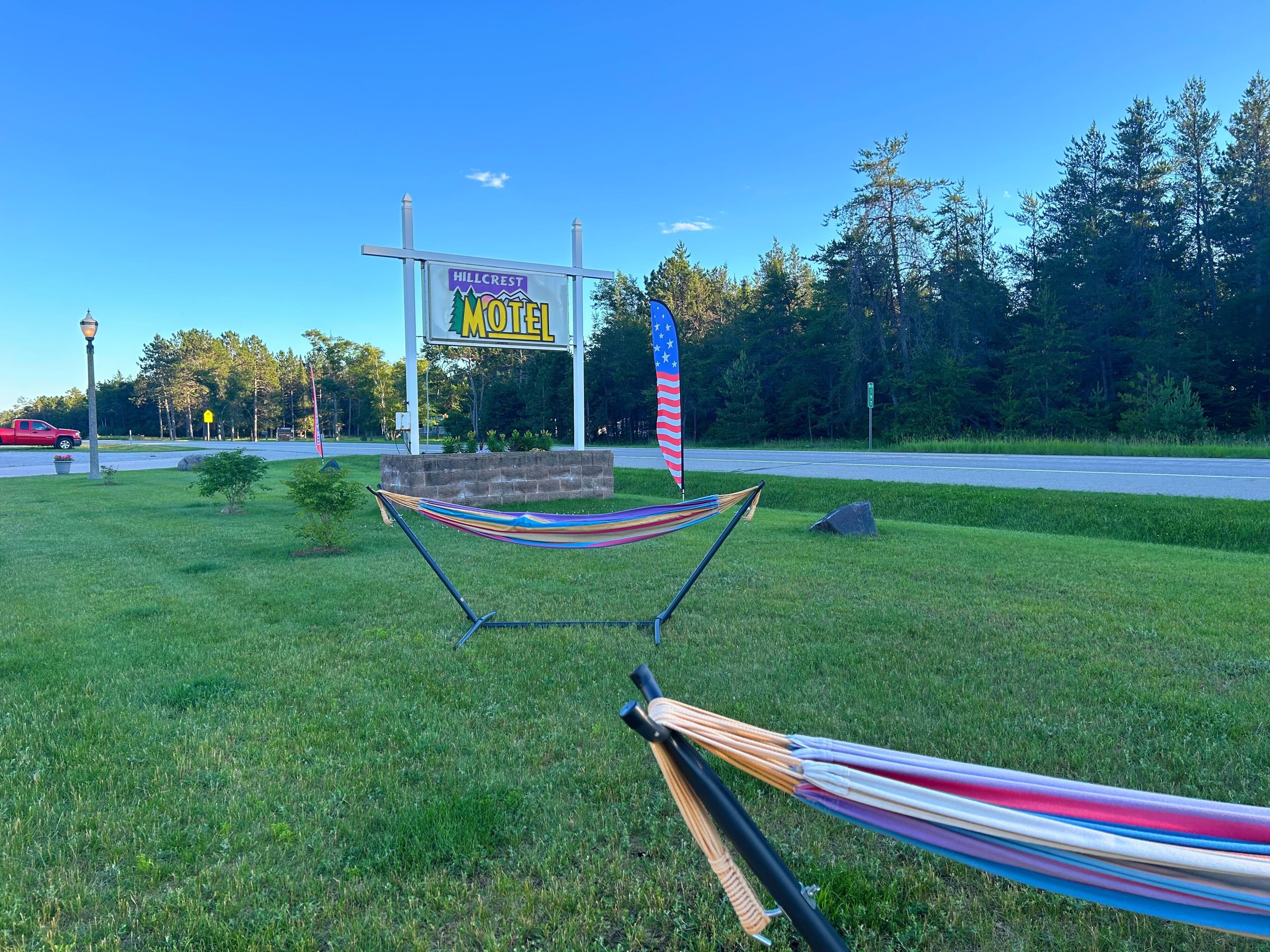 A grassy area with a hammock, a Hillcrest Motel sign, and an American flag.