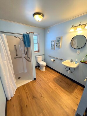 Ein Badezimmer mit Dusche, Toilette und Waschbecken, ausgestattet mit Haltegriffen und einer Handstange.