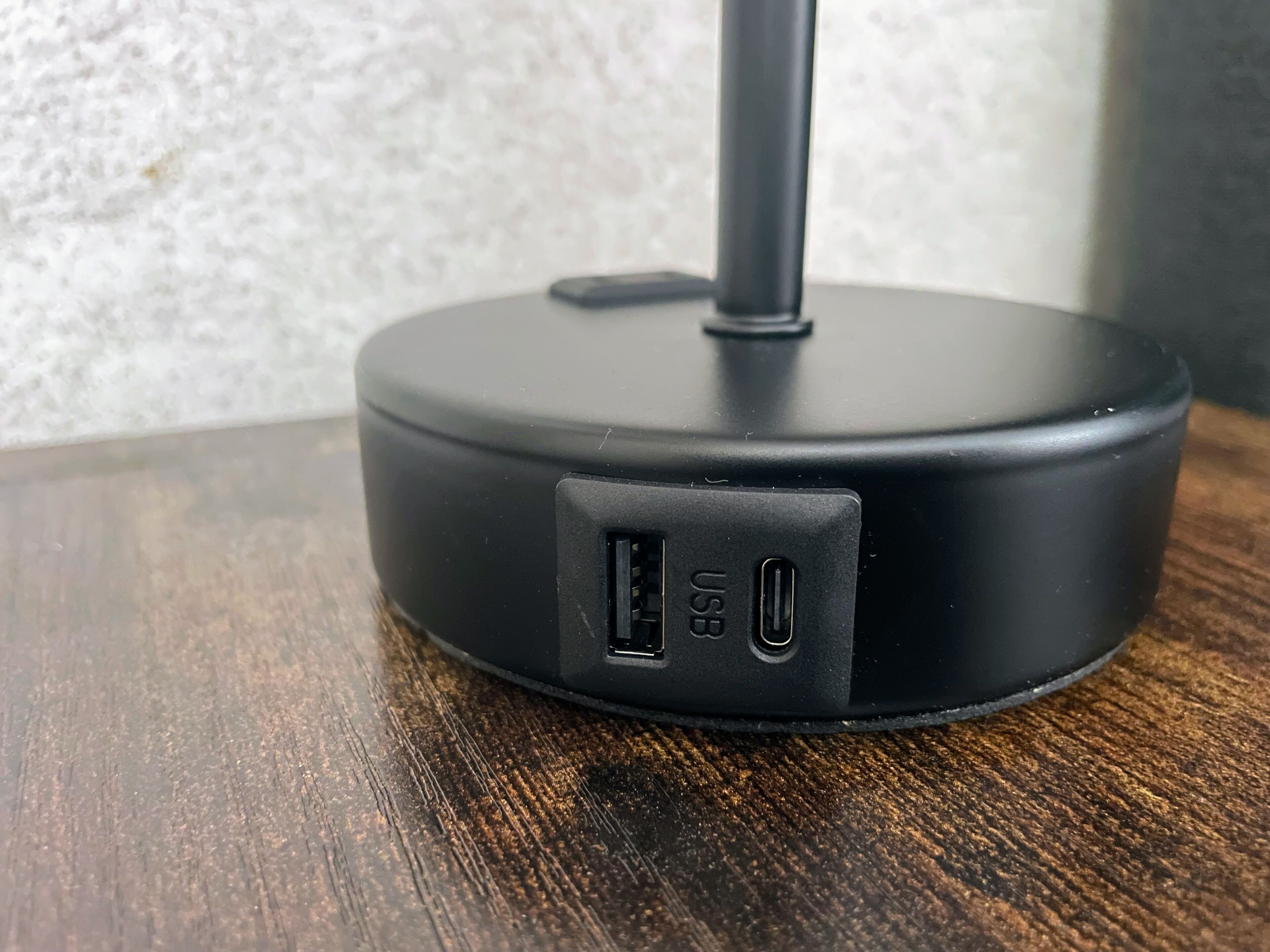 A black wireless charging pad with a USB port and a power button on a wooden surface.