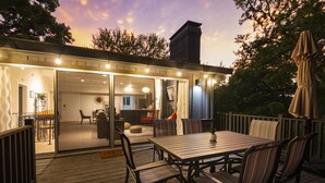 An outdoor deck with a wooden table and chairs, a covered umbrella, and a view of the interior through glass doors. - NEW! ♦ Fun & Modern Lake Retreat ♦ Near Marina! (Pottsboro)