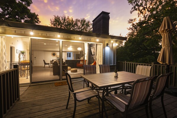 An outdoor deck with a wooden table and chairs, a covered umbrella, and a view of the interior through glass doors. - NEW! ♦ Fun & Modern Lake Retreat ♦ Near Marina! (Pottsboro)