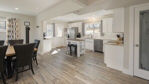 A spacious kitchen with white cabinets, a wooden dining table, and a built-in island with stools. - NEW! ♦ Fun & Modern Lake Retreat ♦ Near Marina! (Pottsboro)