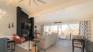 A spacious living room with a fireplace, a sofa, a coffee table, and a dining area with a chess table. - NEW! ♦ Fun & Modern Lake Retreat ♦ Near Marina! (Pottsboro)