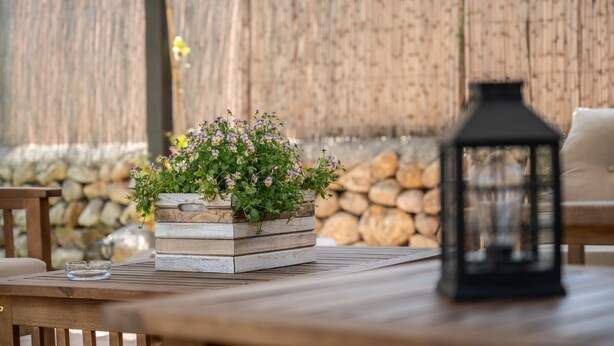 A wooden table with a planter box containing flowers, a lantern, and a stone wall in the background. - Holiday Home Villa Ca Na Campins with Mountain View, Pool, Terraces & Wi-Fi (Campanet)