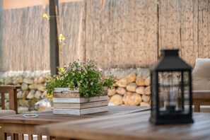 Een houten tafel met een plantenbak met bloemen, een lantaarn en een stenen muur op de achtergrond.