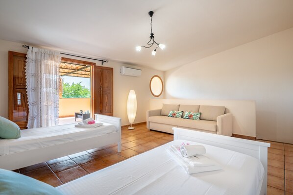 Een slaapkamer met twee bedden, een bank, een plafondlamp en een raam met gordijnen.