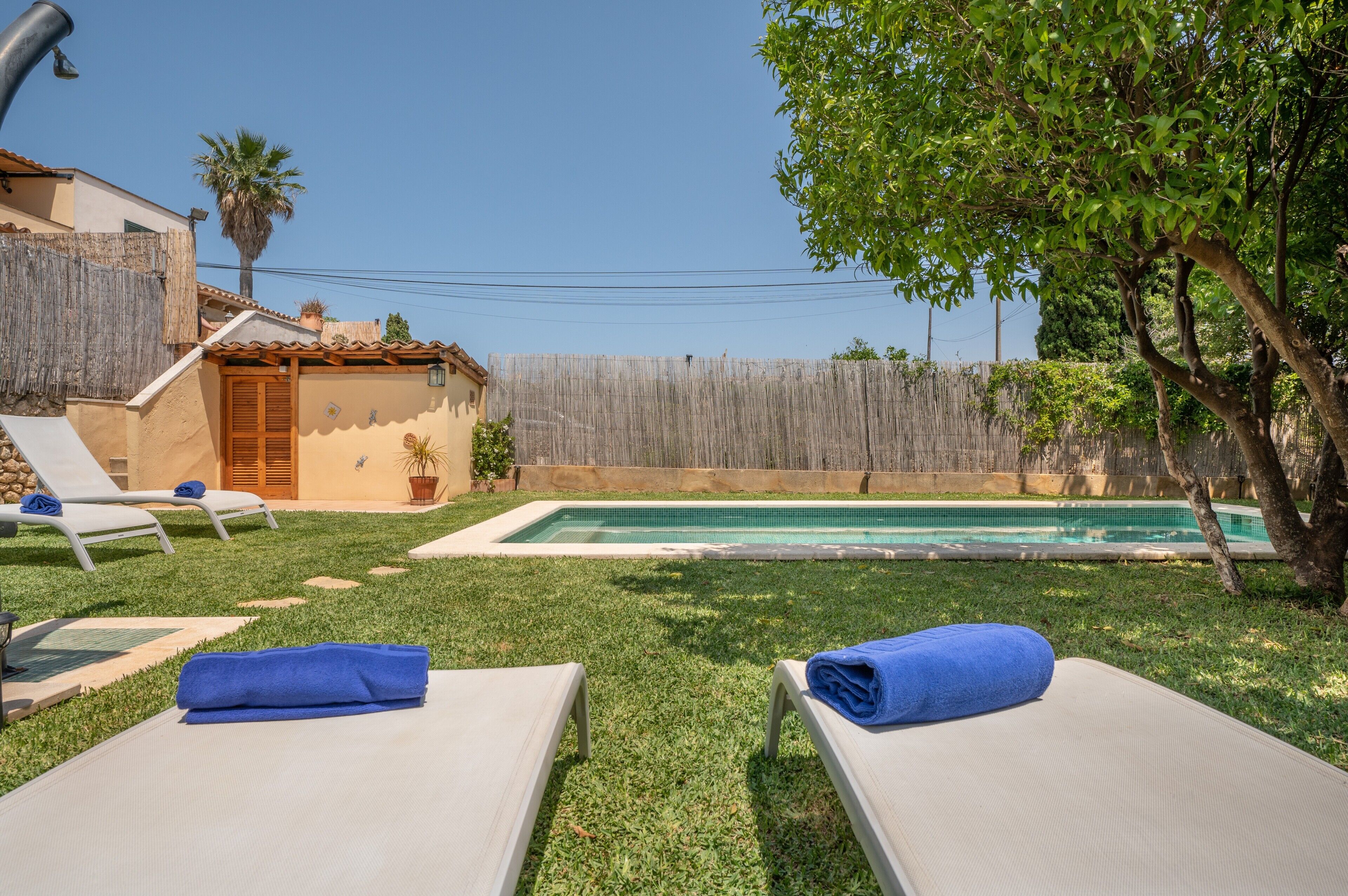 Un patio trasero con piscina, sillas de descanso y valla de madera.