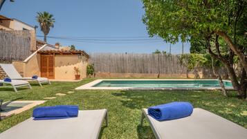 Un patio trasero con piscina, sillas de descanso y valla de madera.