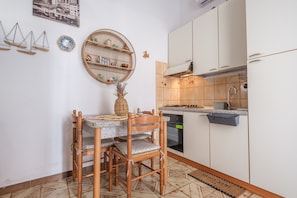 Une cuisine compacte avec des meubles blancs, une cuisinière et un coin repas comprenant une table et des chaises en bois.