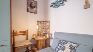 A room with a bed, a chair, a small wooden table with a lamp, and wall decorations including a Buddha image and a fish wall art. - Holiday Home "Tyndaris" with Wi-Fi & Air Conditioning (Oliveri)