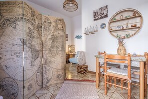 Une pièce comprenant une grande carte du monde, une étagère ronde en bois ornée d’objets décoratifs, une table à manger en bois avec des chaises, et un tapis à motifs.