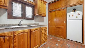Eine Küche mit Holzausstattung, einem weißen Kühlschrank und einem Fenster mit Jalousien.