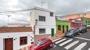 Straßenansicht mit einem roten Auto vor einem Fußgängerüberweg, Gebäuden mit Hausnummern und einem sichtbaren Ladenlokal.