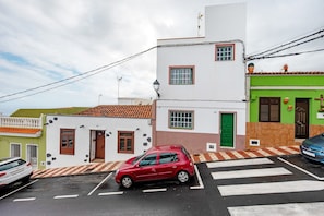 A red car parked in a street with a crosswalk, buildings with different colored facades, and a clear sky.