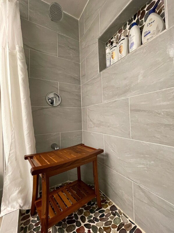Un espace douche avec des carreaux gris, une étagère en bois où sont rangés les produits de toilette et un rideau de douche.