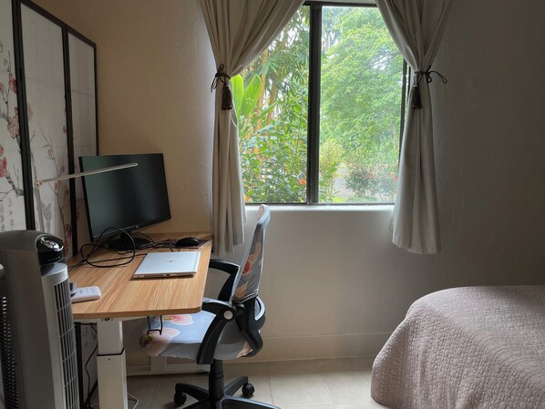 Ein Zimmer mit Schreibtisch, Computer, Stuhl und Bett.