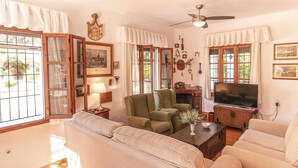 Ein Wohnzimmer mit einer Couch, Sesseln, einem Fernseher und einem Deckenventilator.