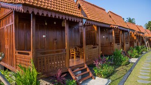 A row of wooden cabins with tiled roofs, wooden railings, and a paved pathway with stepping stones.