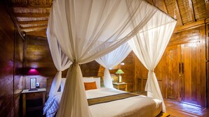 A wooden cabin bedroom with a four-poster bed, a nightstand, a lamp, and a wooden door.