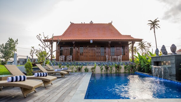 A traditional building with a tiled roof, a pool with a waterfall feature, and lounge chairs on a wooden deck.