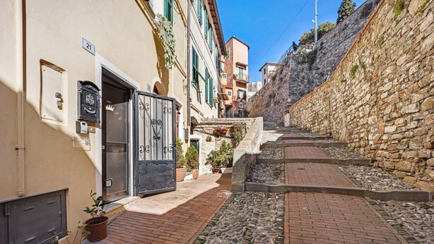Eine enge Gasse mit Steinmauern, einem gepflasterten Weg und Gebäuden mit Fenstern und Türen.