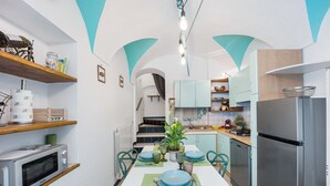 Eine moderne Küche mit Essbereich, Edelstahlgeräten, türkisfarbenen Akzenten und einer Treppe zu einer oberen Ebene.
