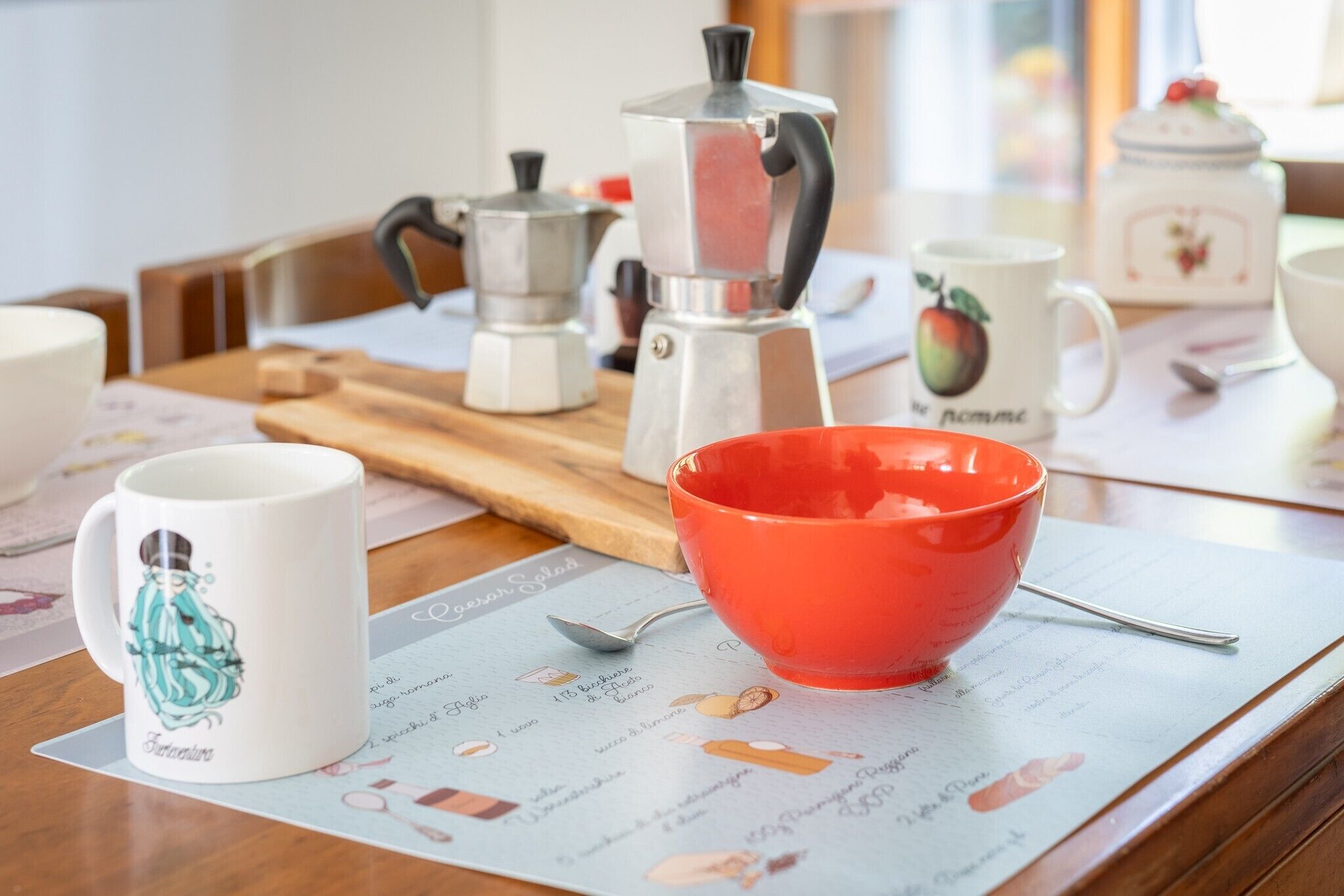 A kitchen counter with a coffee maker, a red bowl, and a spoon on a placemat.