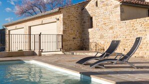 A stone building with a swimming pool and lounge chairs.