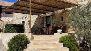 A stone building with a covered outdoor seating area and steps leading to a door.