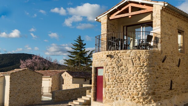 A stone building with a balcony, a red door, and a staircase leading to the entrance.
