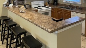 A kitchen with wooden cabinets, a white microwave, a stove, a sink, and a window with blinds.