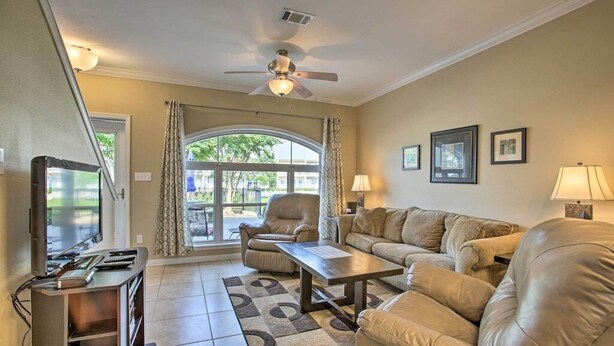 A living room with a sofa, armchair, coffee table, TV, and a ceiling fan.