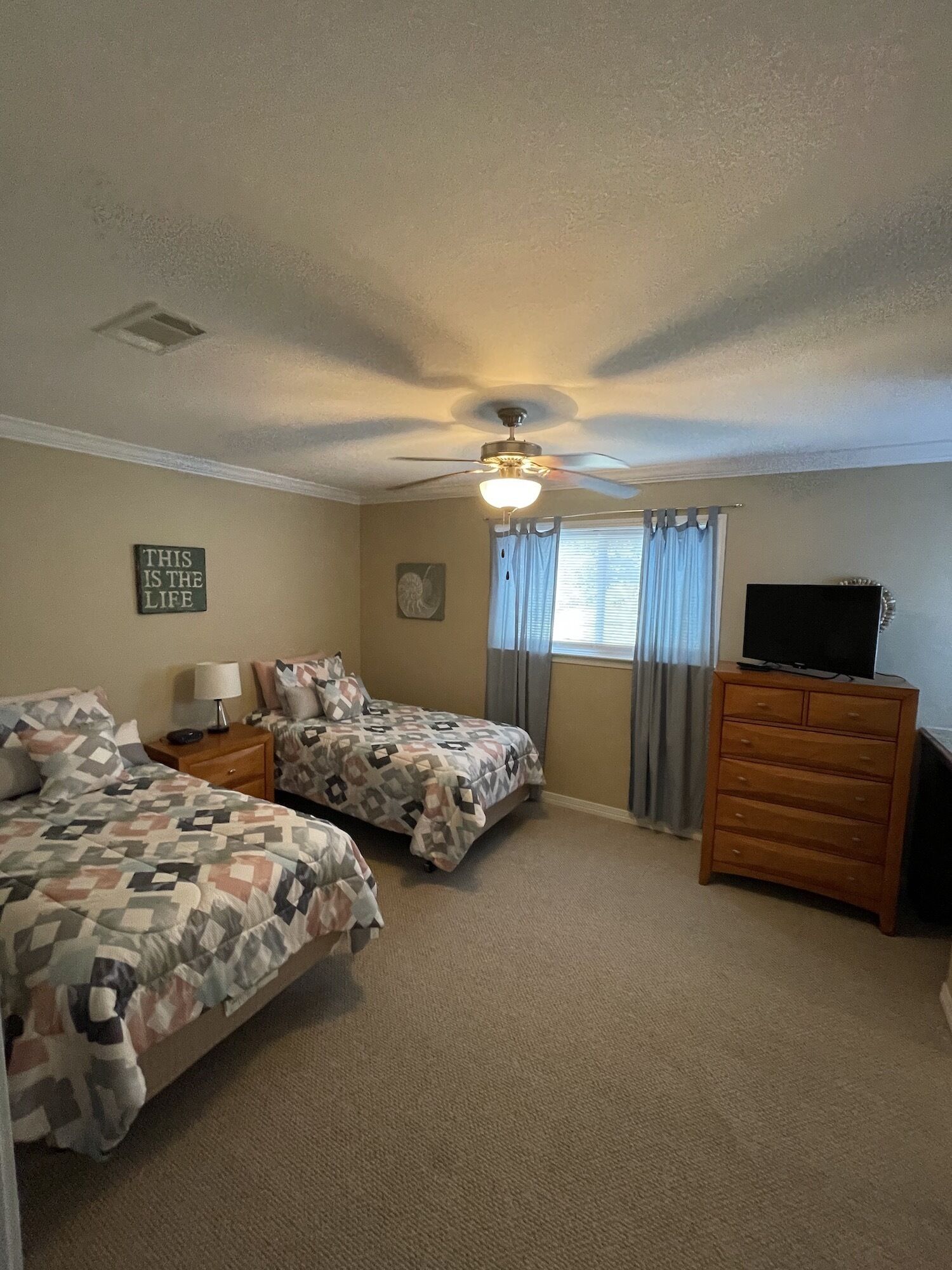 A bedroom with two beds, a ceiling fan, a dresser, and a television.
