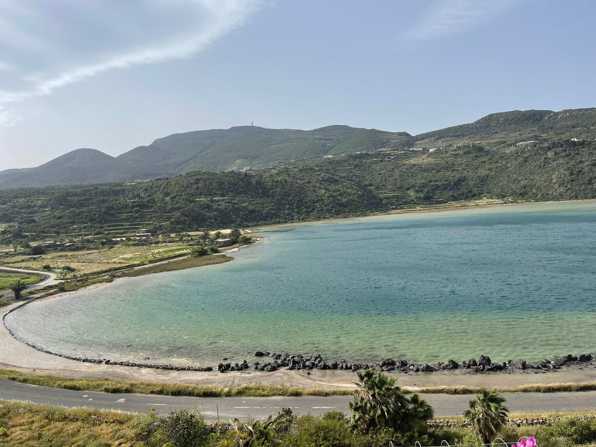 A coastal landscape with a clear view of the sea, a curved road, and a rocky shoreline.