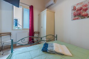 Une chambre à coucher avec un lit, une armoire, une fenêtre avec un rideau rouge, une chaise et un tableau accroché au mur.