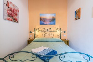 A bedroom with a bed, a painting of a beach scene, and a wall-mounted lamp.
