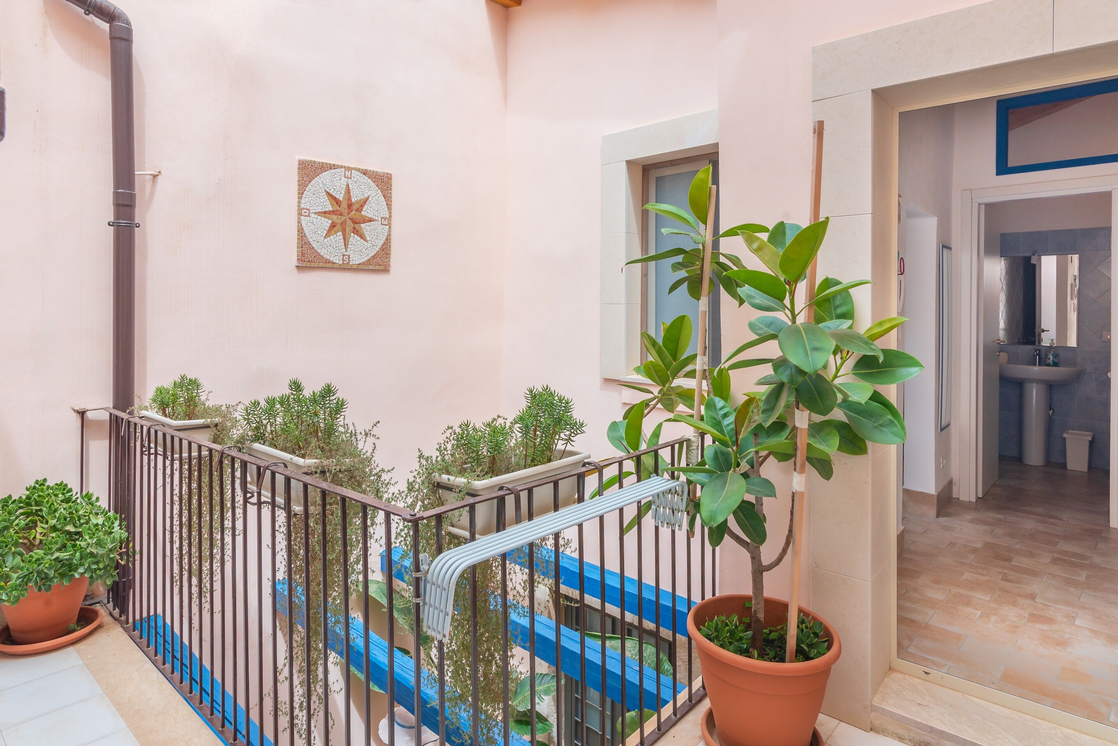 Ein Balkon mit Blumentöpfen, einem blauen Wasserspiel und einem gefliesten Boden.