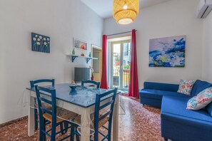 Un salon avec un canapé bleu, une table à manger avec des chaises, un téléviseur et des œuvres d’art accrochées aux murs.