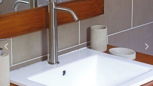 Un lavabo de salle de bain avec un robinet moderne, un miroir au-dessus et deux serviettes enroulées posées sur le comptoir.