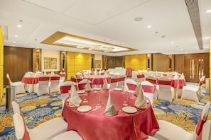 A conference room with round tables, white chairs, and red tablecloths.