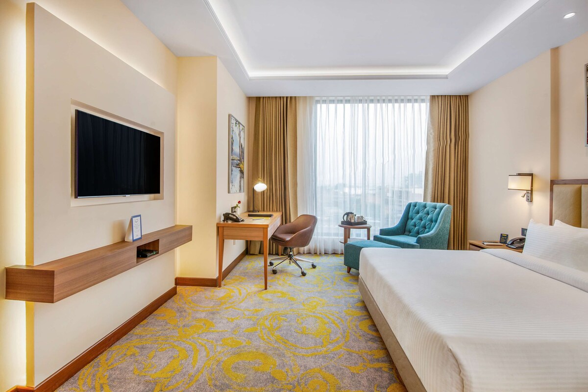 Une chambre d’hôtel équipée d’un lit, d’un bureau, d’une chaise et d’un téléviseur fixé au mur.