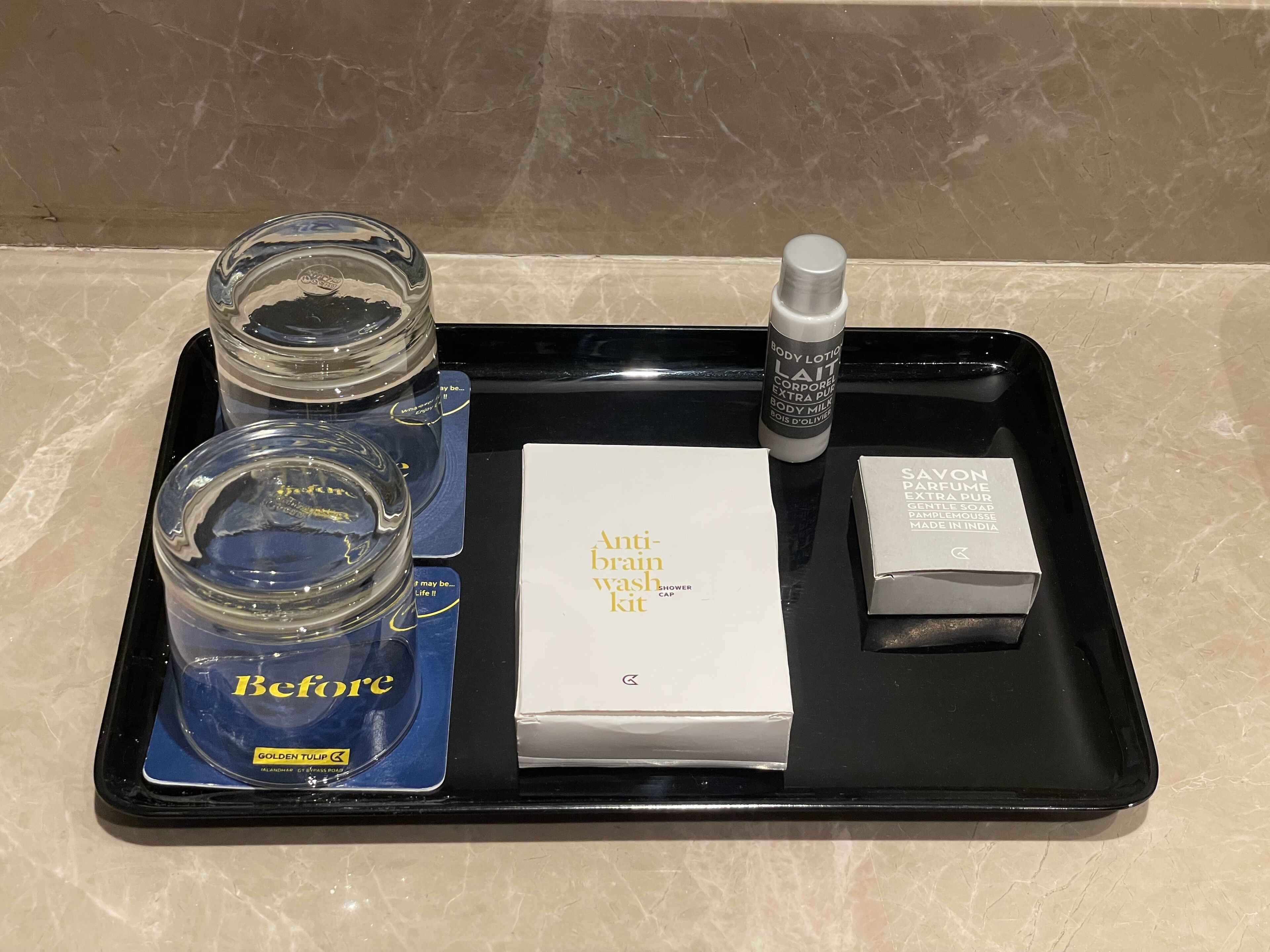 Un plateau contenant une lotion pour le corps, un bonnet de douche, une boîte de savon et deux pots de gel douche « Before ».