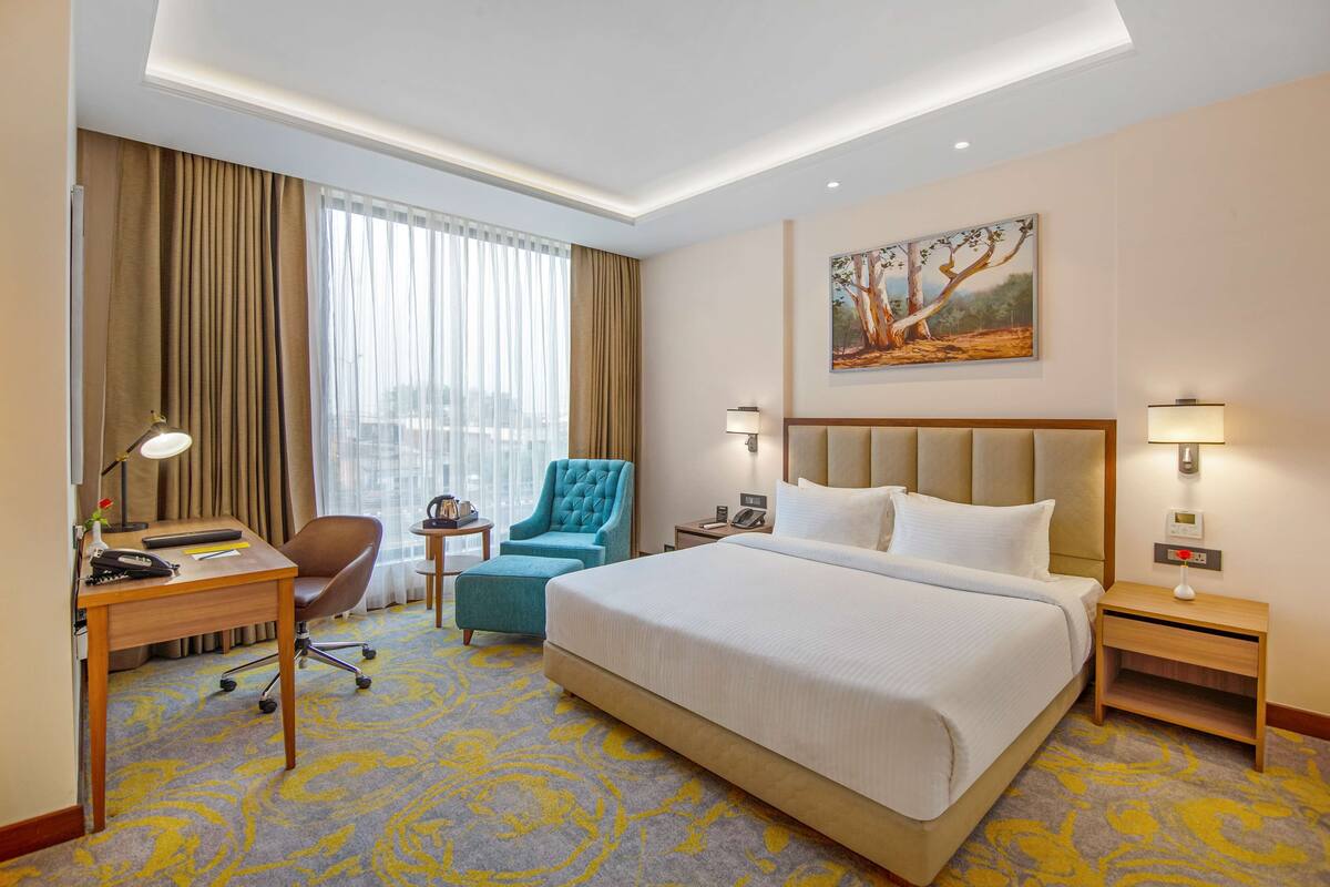 Ein Hotelzimmer mit einem großen Bett, einem Schreibtisch mit Lampe, einem Sessel, einem kleinen Tisch und einem Nachttisch mit Lampe.