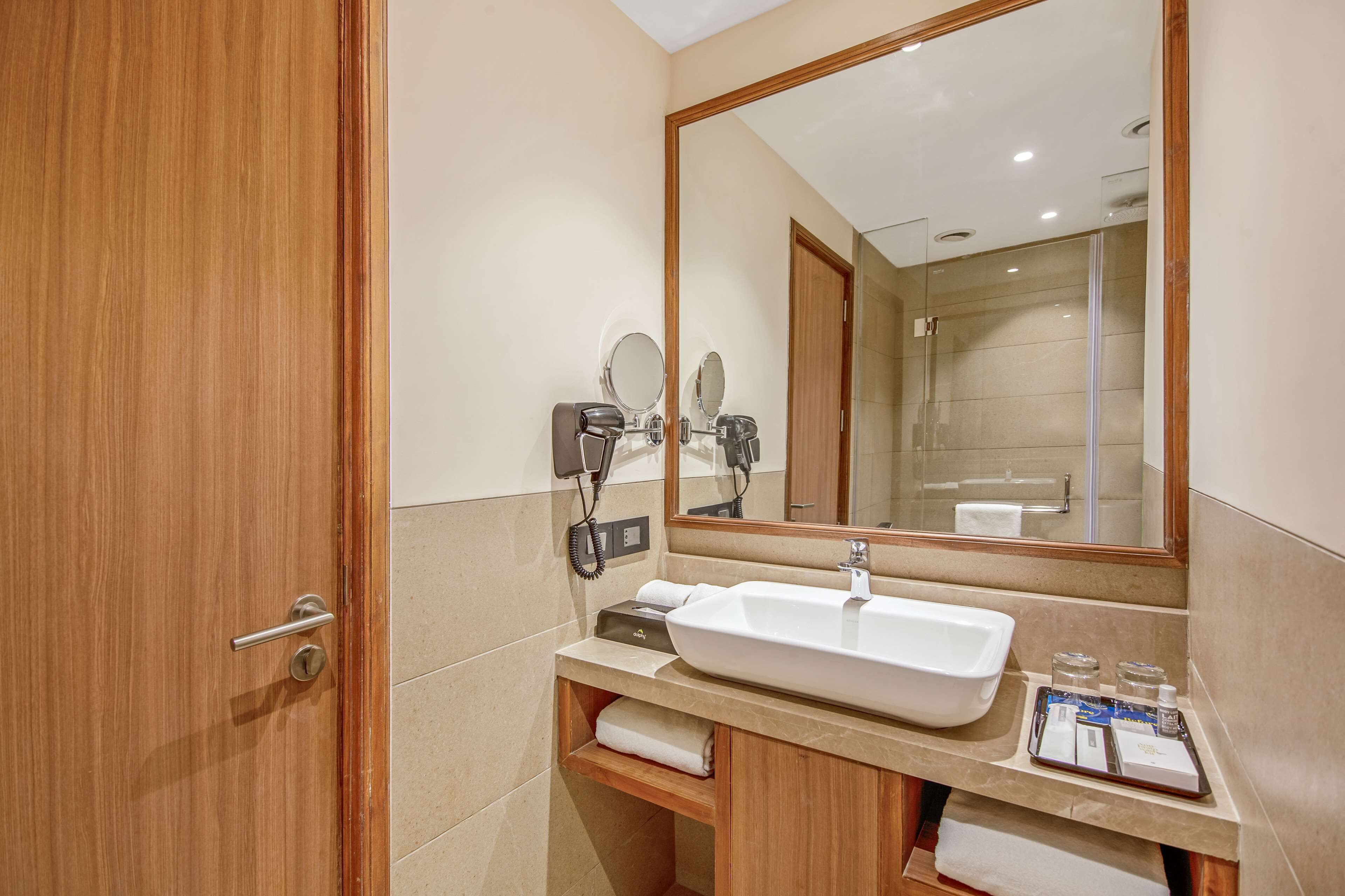 Un baño de hotel con una puerta de madera, un lavabo blanco, un espejo grande y un perchero para toallas.