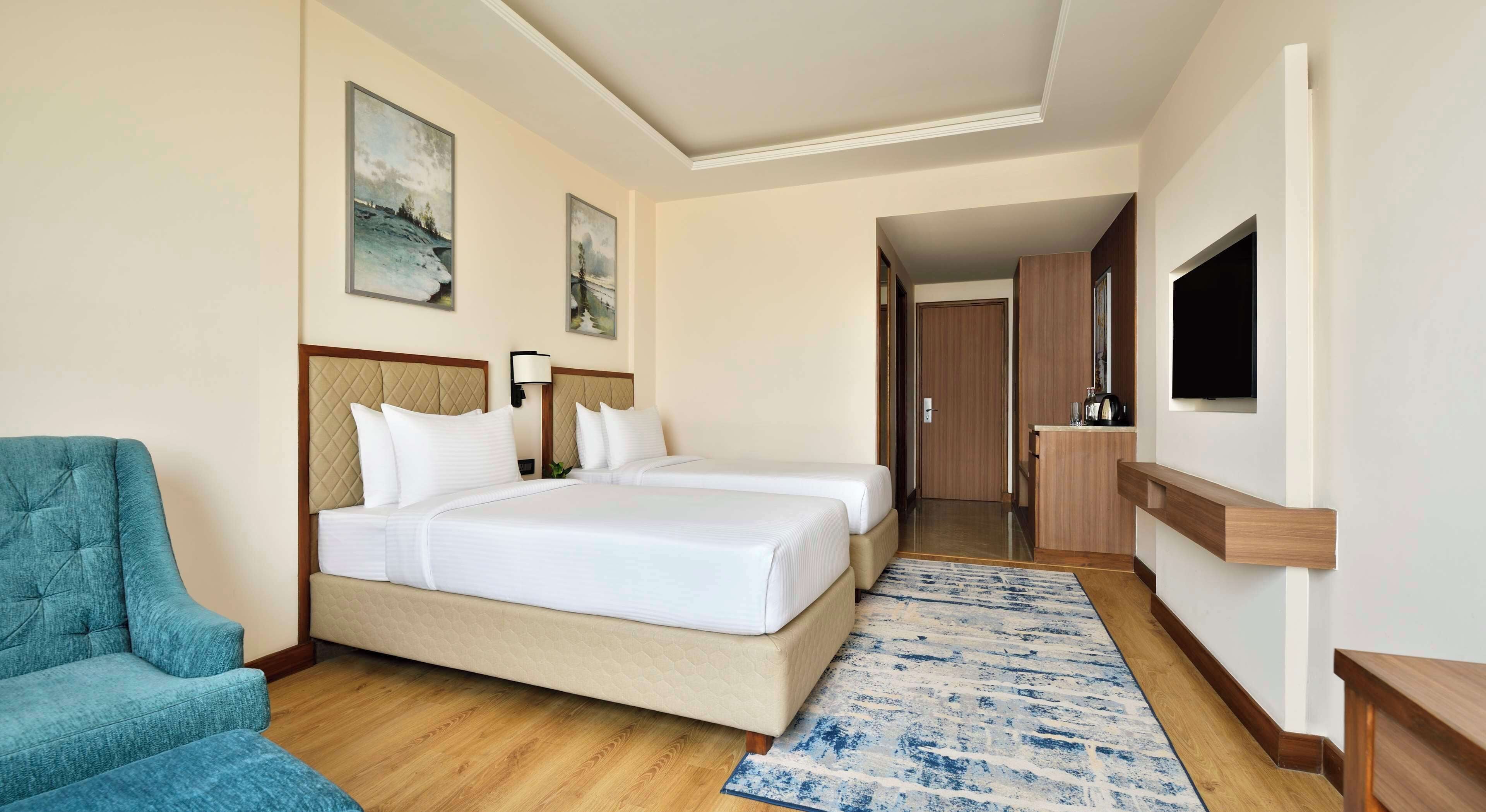 A hotel room with a bed, a chair, a TV, and artwork on the walls.
