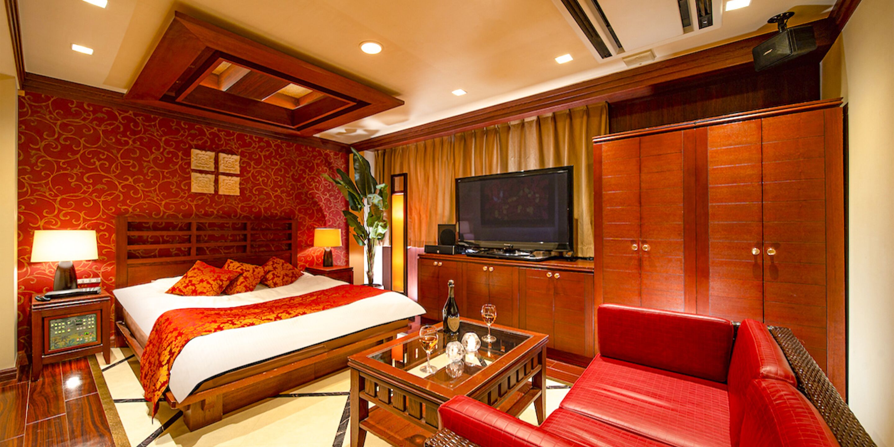 A hotel room with a large bed, a television, a red sofa, and a wooden cabinet.