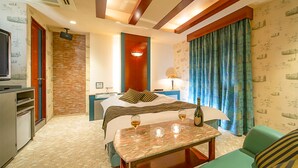Habitación de hotel con cama, una mesa con una botella y vasos, televisión y ventana con cortinas.