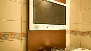 Un baño público con un secador de manos sobre un lavamanos, paredes de azulejos y un detalle decorativo en la base de la pared.